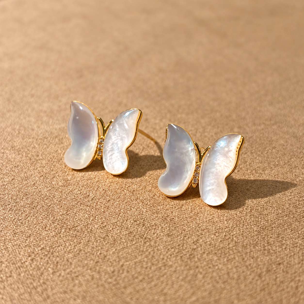 Pair of butterfly mother-of-pearl earrings resting on textured paper